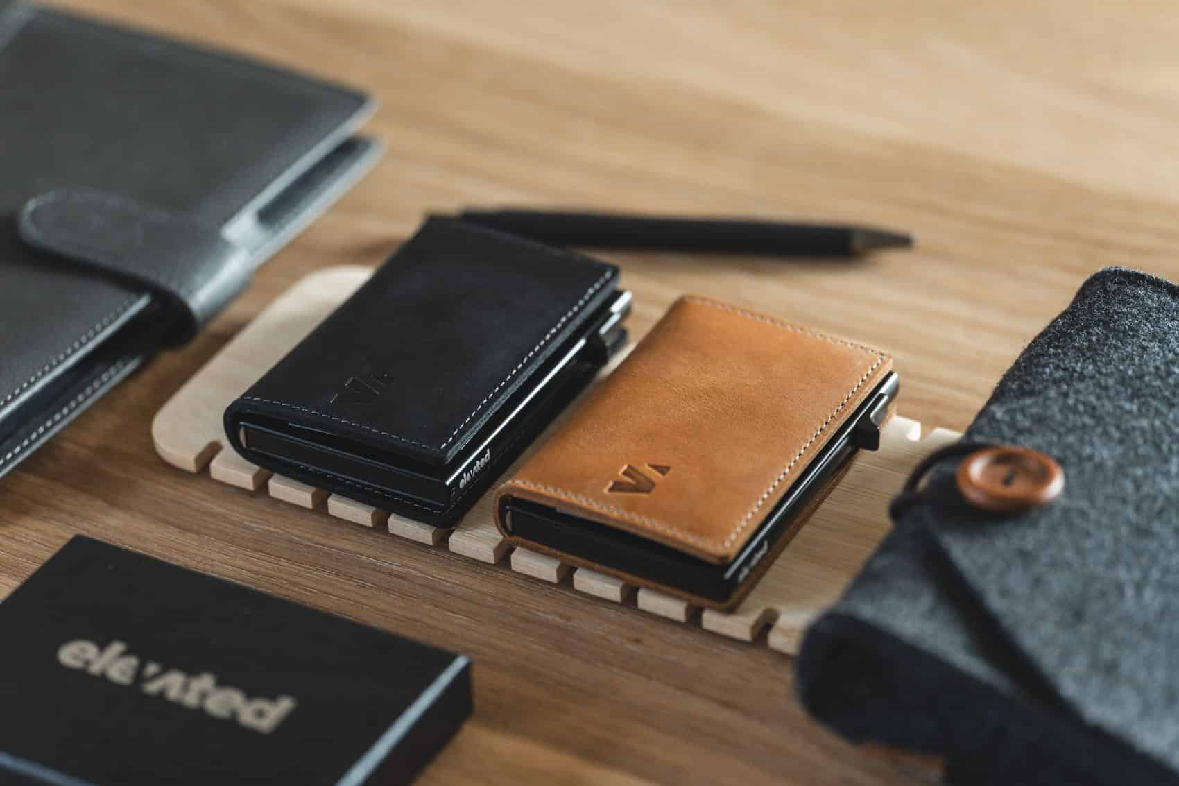 Kvaliteetsest nahast valmistatud Elevated Slim Wallet 2.0, esitletud helepruunis ja mustas värvivalikus puidust taustal